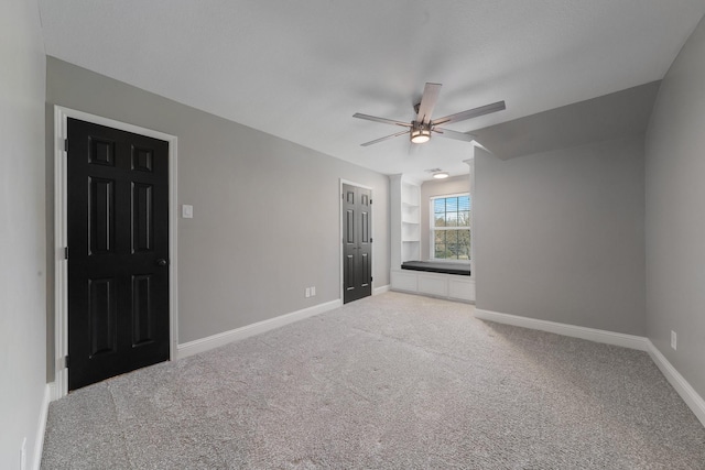 carpeted spare room with built in shelves and ceiling fan