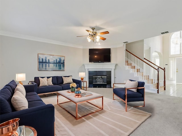 living room featuring ceiling fan, crown molding, light carpet, and a tiled fireplace