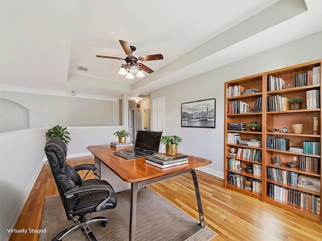 office area with light wood-type flooring, a raised ceiling, and ceiling fan