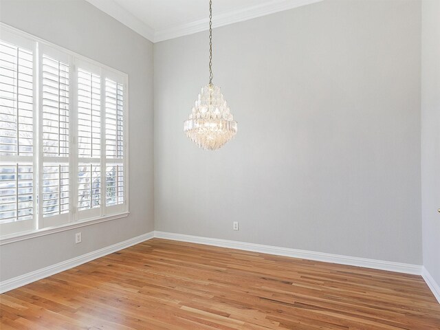 empty room with plenty of natural light, light hardwood / wood-style floors, crown molding, and an inviting chandelier