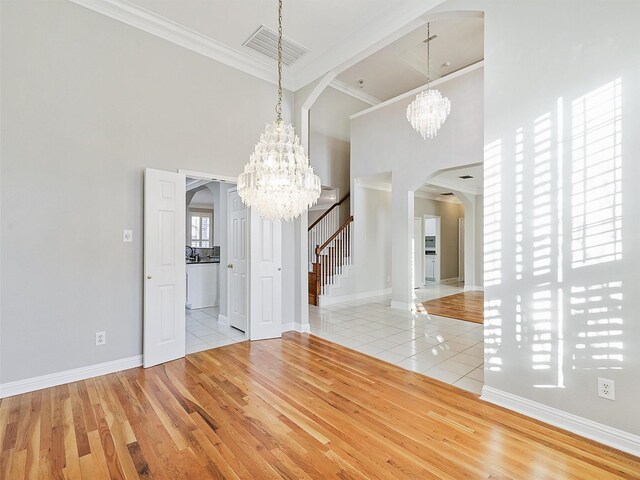 unfurnished dining area with a notable chandelier, light tile patterned floors, crown molding, and a towering ceiling