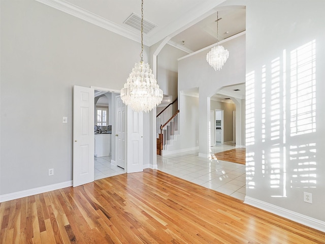 unfurnished dining area featuring ornamental molding, a towering ceiling, a notable chandelier, and light hardwood / wood-style floors