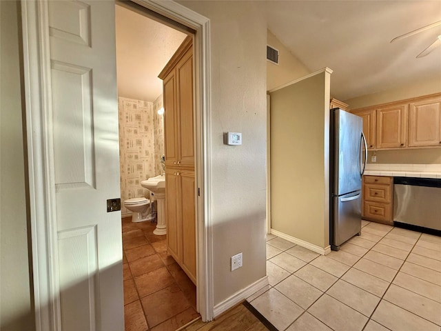 kitchen featuring ceiling fan, light brown cabinetry, light tile patterned flooring, and stainless steel appliances