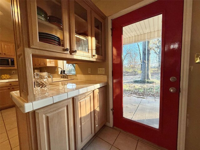 kitchen featuring tile countertops, glass insert cabinets, and a sink