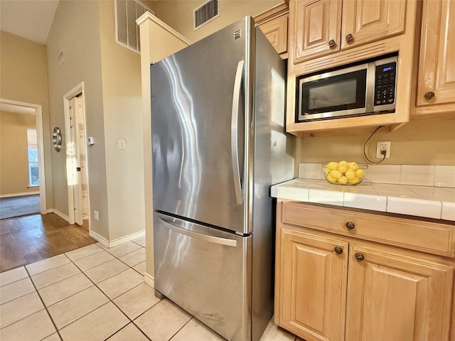 kitchen with tile counters, light tile patterned flooring, and appliances with stainless steel finishes