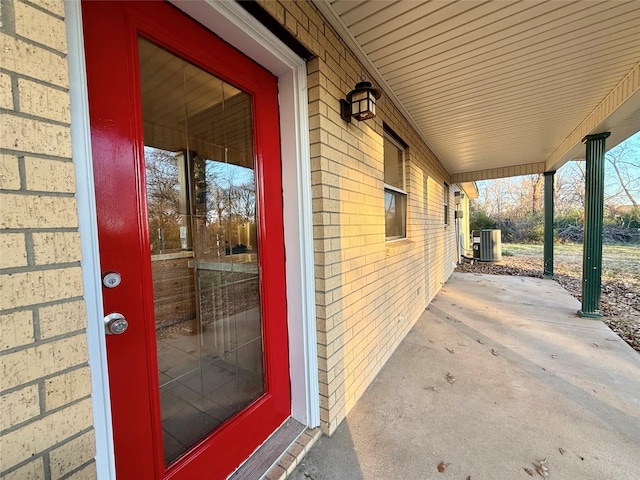 entrance to property with central air condition unit, brick siding, and a porch