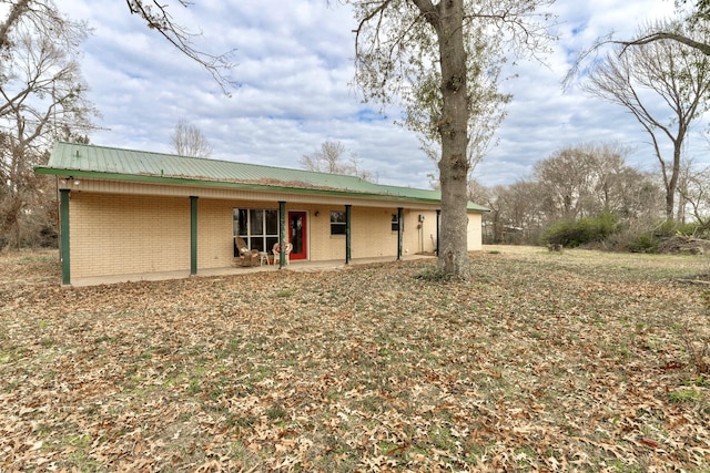 back of property featuring metal roof, a patio, and brick siding