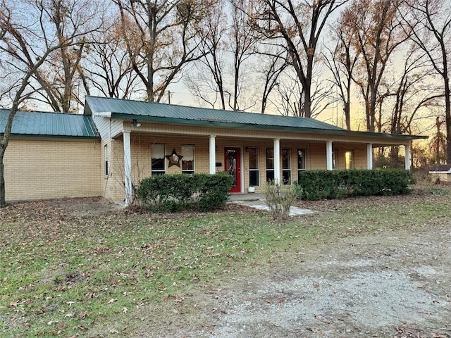 view of front of home with a porch, brick siding, and metal roof