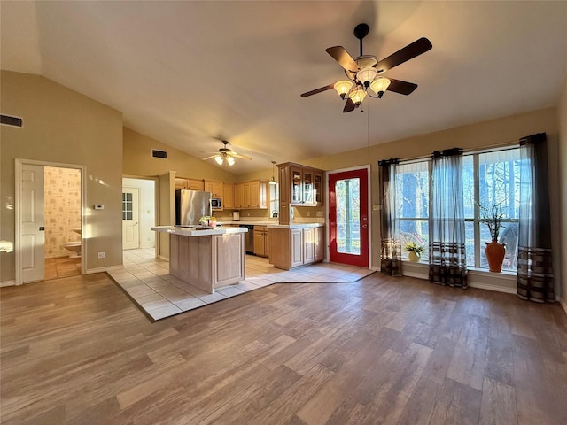 kitchen with a center island, stainless steel appliances, light wood-style floors, light countertops, and vaulted ceiling