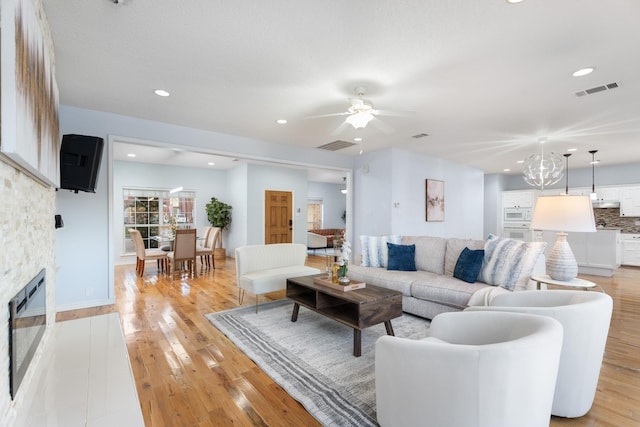 living room featuring light wood-type flooring, a stone fireplace, and ceiling fan