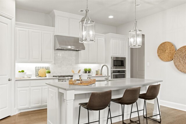 kitchen featuring a center island with sink, white cabinetry, stainless steel appliances, and range hood