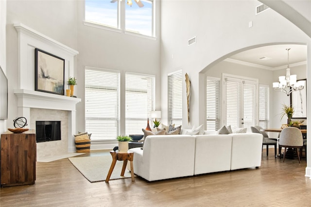 living room featuring an inviting chandelier, a high end fireplace, crown molding, a towering ceiling, and light hardwood / wood-style floors