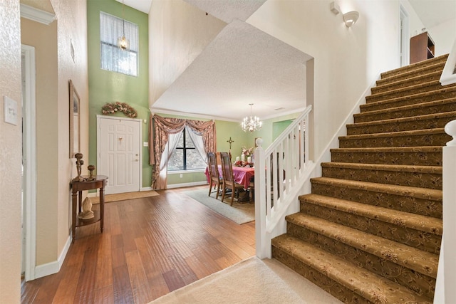 foyer entrance featuring an inviting chandelier, wood-type flooring, ornamental molding, and a high ceiling