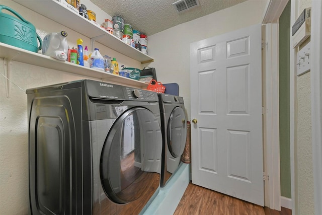 clothes washing area with wood-type flooring, a textured ceiling, and washer and clothes dryer