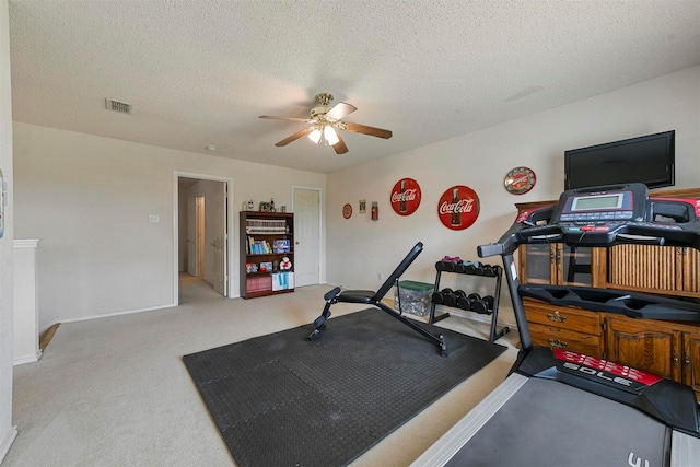 exercise area with ceiling fan, light colored carpet, and a textured ceiling