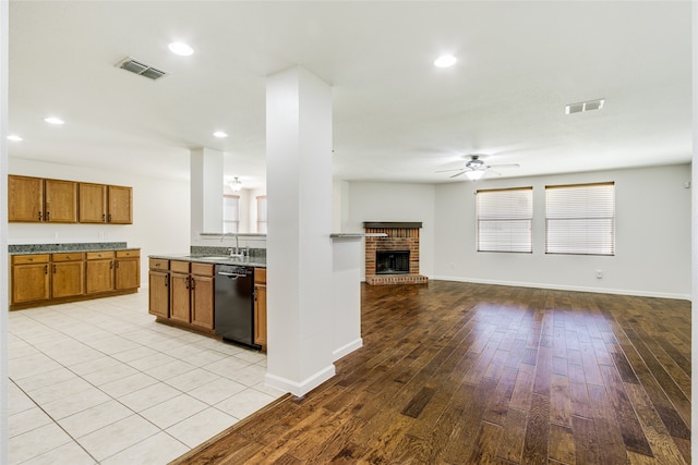 kitchen featuring a brick fireplace, ceiling fan, light hardwood / wood-style floors, and black dishwasher