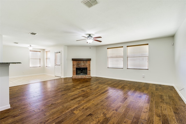 unfurnished living room with ceiling fan, a fireplace, and dark wood-type flooring