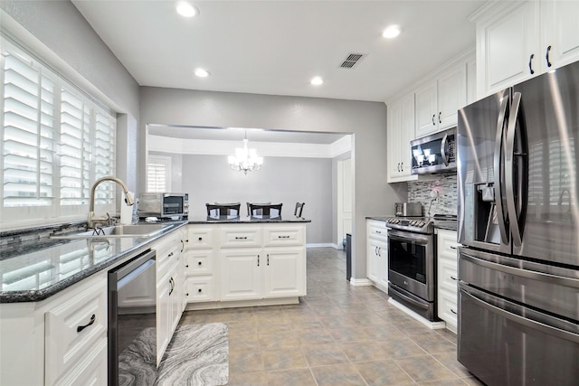 kitchen with a sink, backsplash, dark stone counters, appliances with stainless steel finishes, and white cabinets