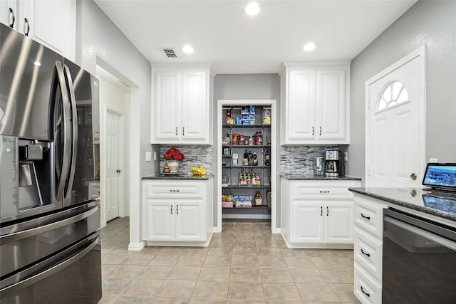 kitchen with dark stone countertops, visible vents, stainless steel fridge, and tasteful backsplash