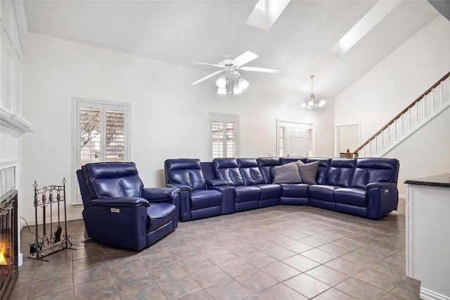 living area with high vaulted ceiling, a skylight, stairs, tile patterned flooring, and a glass covered fireplace