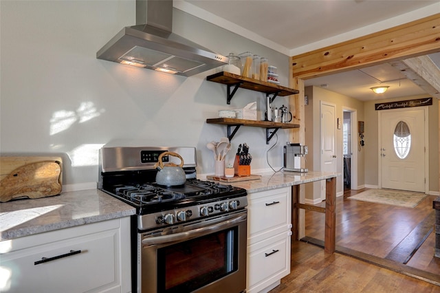 kitchen with wall chimney range hood, light hardwood / wood-style flooring, gas range, light stone countertops, and white cabinetry