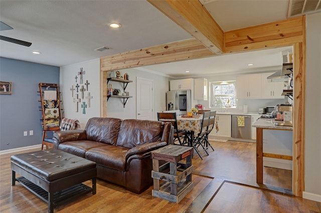 living room featuring beamed ceiling, light wood-type flooring, ceiling fan, and sink