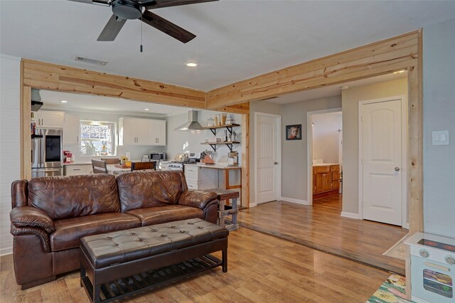 living room with beamed ceiling, ceiling fan, and light wood-type flooring