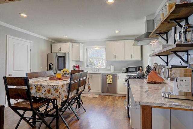 kitchen with wall chimney exhaust hood, appliances with stainless steel finishes, light wood-type flooring, white cabinets, and ornamental molding