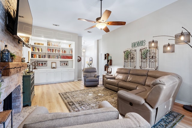 living room with ceiling fan, a fireplace, built in features, and light wood-type flooring