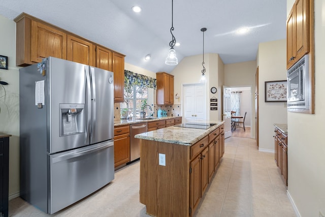 kitchen with lofted ceiling, sink, appliances with stainless steel finishes, decorative light fixtures, and a kitchen island