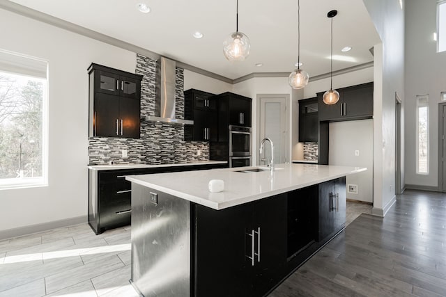 kitchen featuring an island with sink, wall chimney exhaust hood, crown molding, and hanging light fixtures