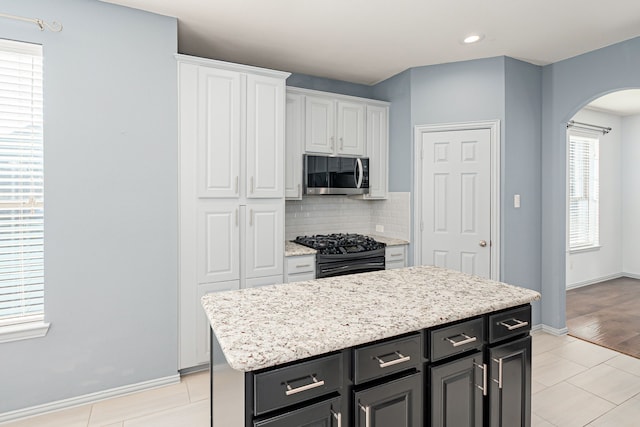 kitchen with black gas range, white cabinetry, light tile patterned floors, tasteful backsplash, and a kitchen island