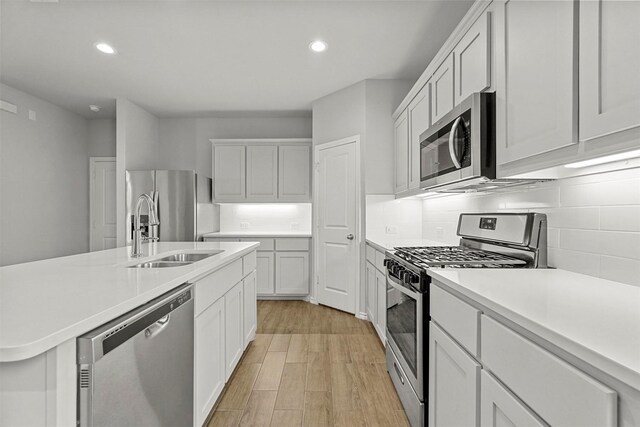 kitchen with appliances with stainless steel finishes, white cabinetry, sink, decorative backsplash, and light hardwood / wood-style flooring