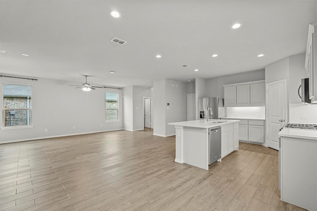 kitchen with white cabinetry, sink, ceiling fan, stainless steel appliances, and an island with sink