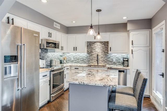 kitchen with stainless steel appliances, a kitchen island, pendant lighting, and white cabinets