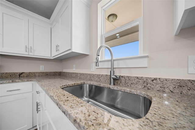 kitchen featuring light stone countertops, white cabinetry, and sink