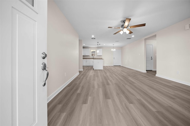 unfurnished living room featuring ceiling fan with notable chandelier and light hardwood / wood-style floors