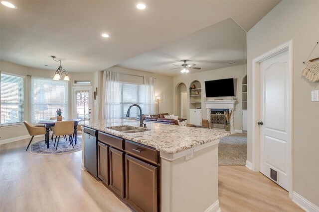 kitchen featuring dishwasher, ceiling fan with notable chandelier, sink, built in features, and an island with sink