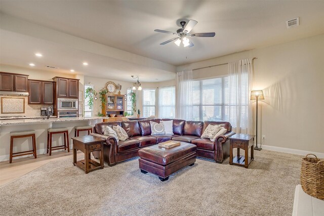 living room with ceiling fan with notable chandelier and sink