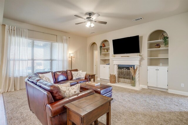 carpeted living room featuring built in shelves and ceiling fan