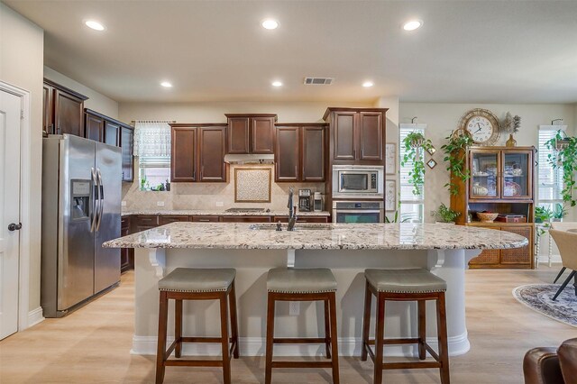 kitchen with decorative backsplash, appliances with stainless steel finishes, light stone countertops, sink, and a center island with sink