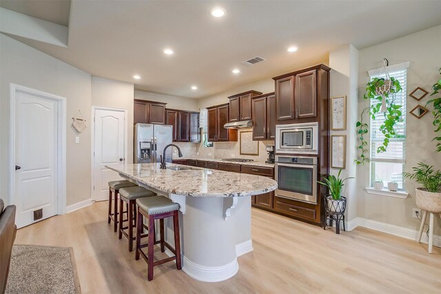 kitchen featuring sink, light hardwood / wood-style floors, a center island with sink, and appliances with stainless steel finishes