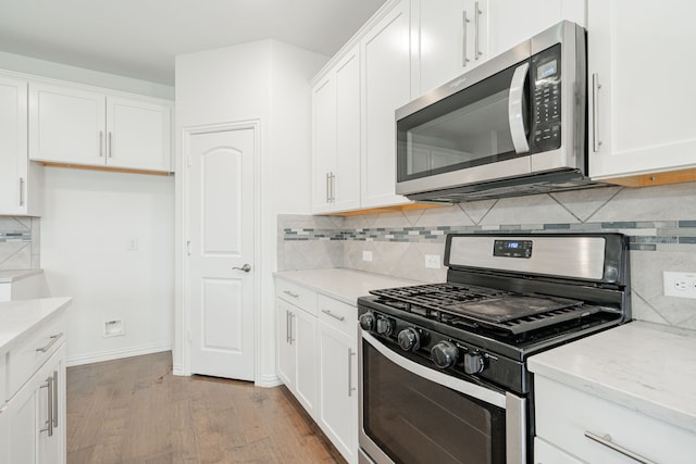 kitchen with stainless steel appliances, tasteful backsplash, light stone counters, light hardwood / wood-style floors, and white cabinets