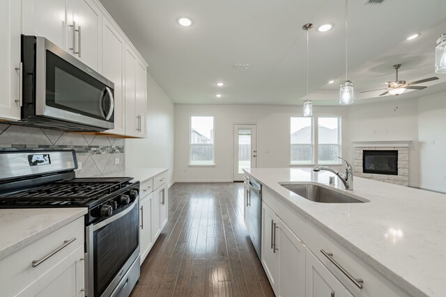 kitchen with appliances with stainless steel finishes, sink, decorative light fixtures, white cabinetry, and a stone fireplace