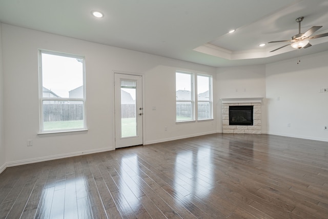 unfurnished living room with a raised ceiling, ceiling fan, dark wood-type flooring, crown molding, and a fireplace