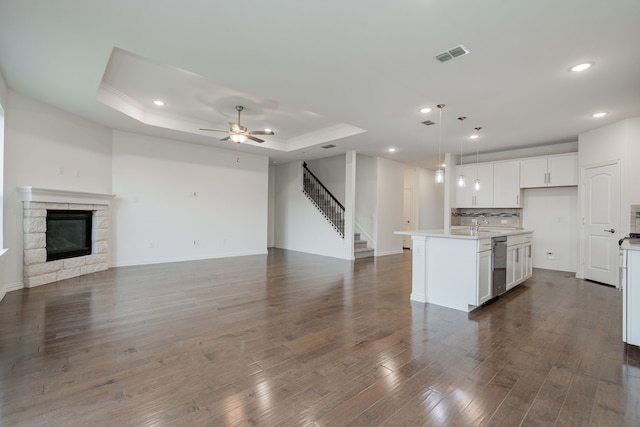 kitchen with a center island with sink, decorative light fixtures, a raised ceiling, and white cabinetry