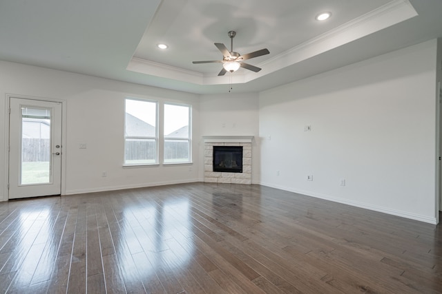 unfurnished living room featuring ceiling fan, a stone fireplace, a raised ceiling, and dark wood-type flooring