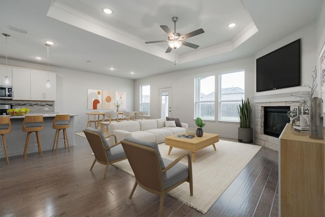 living room with dark hardwood / wood-style flooring, ornamental molding, a raised ceiling, ceiling fan, and a fireplace