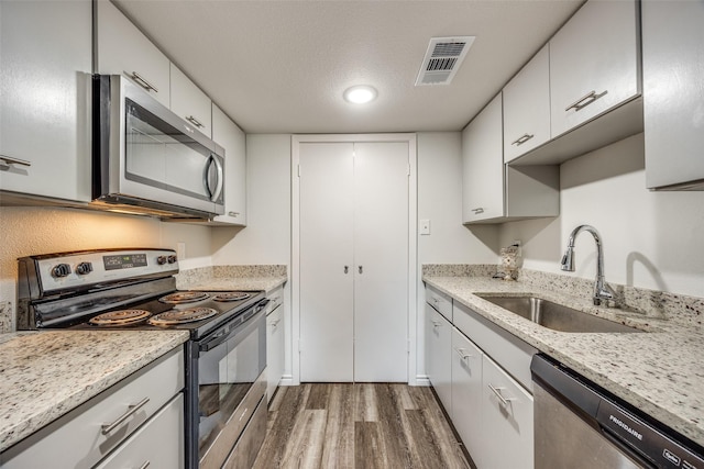 kitchen with light stone counters, sink, white cabinetry, and stainless steel appliances