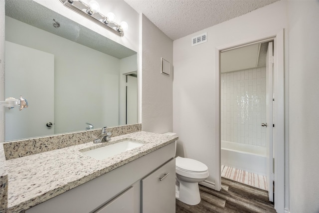 full bathroom featuring tiled shower / bath combo, wood-type flooring, a textured ceiling, toilet, and vanity